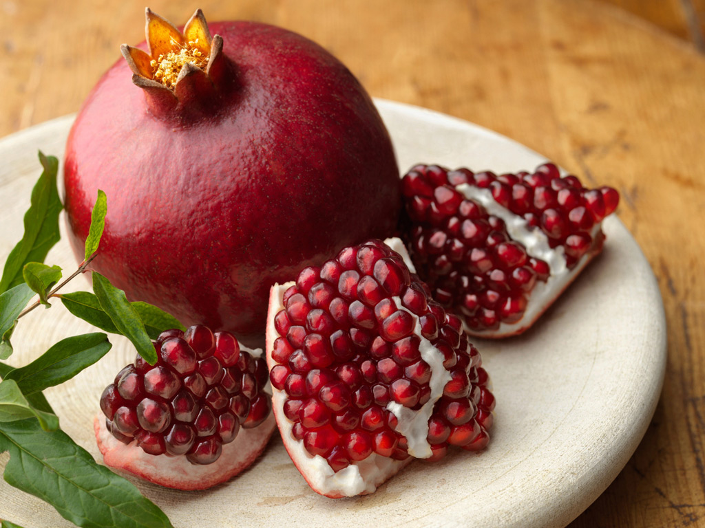Image of pomegranate on a plate with another pomegranate cut in portions so the seeds are visible.