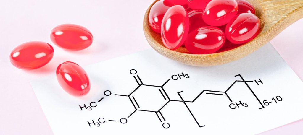 Image of a spoon containing several red gel capsules and a paper that displays the schematic structure of the Coenzyme Q10 molecule.
