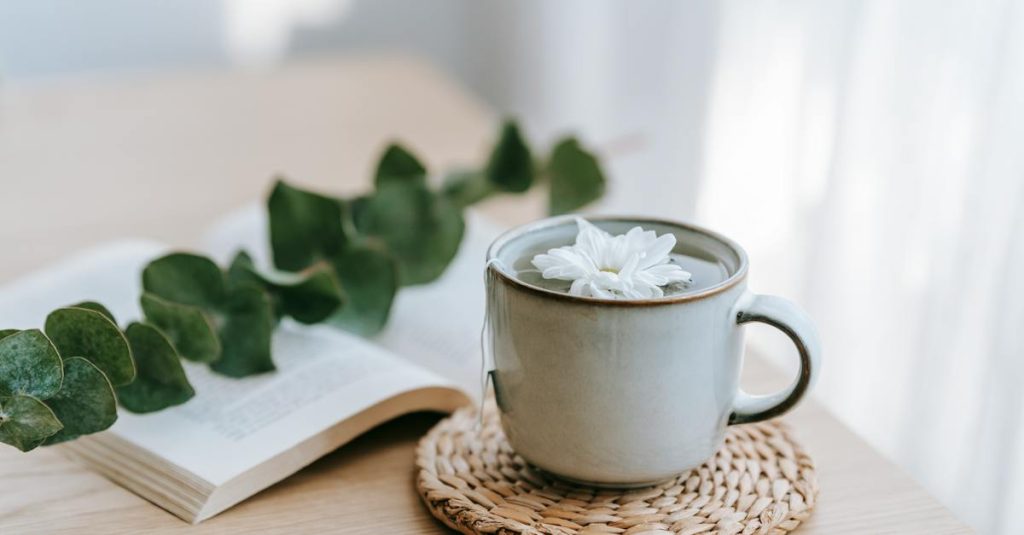 Image of a cup of green tea on a table, with some green tea leaves in the background on the table.
